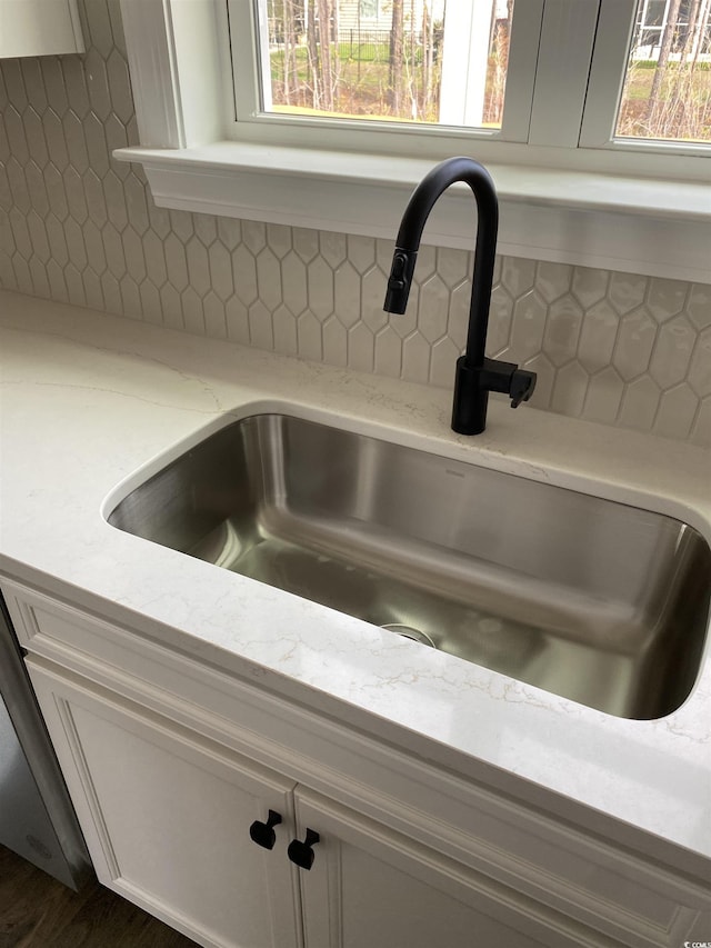 kitchen view of a sink, decorative backsplash, light stone countertops, and white cabinets