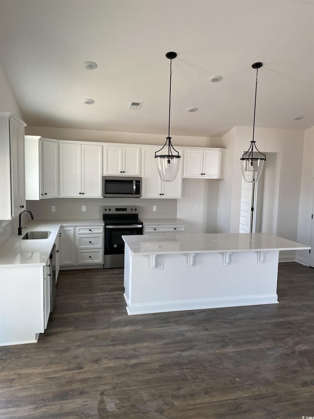 kitchen with stainless steel appliances, a sink, dark wood-style flooring, white cabinetry, and tasteful backsplash