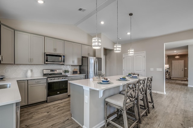 kitchen featuring gray cabinets, light wood finished floors, a kitchen breakfast bar, and stainless steel appliances