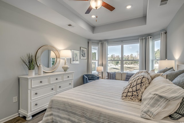 bedroom with visible vents, baseboards, wood finished floors, and a tray ceiling