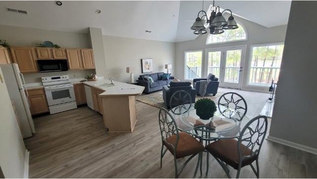 kitchen with light wood-style flooring, a peninsula, white appliances, open floor plan, and light brown cabinetry