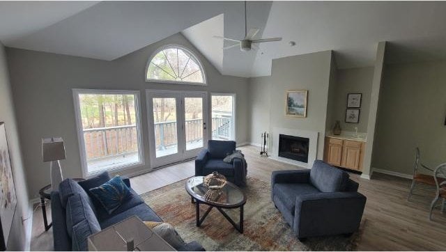 living area with baseboards, wood finished floors, french doors, a fireplace, and high vaulted ceiling