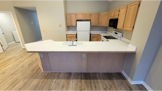 kitchen with white appliances, kitchen peninsula, sink, and light wood-type flooring