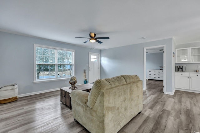 living room featuring crown molding, wood finished floors, a ceiling fan, and baseboards