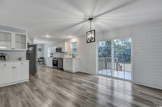 kitchen with wood finished floors, light countertops, stainless steel appliances, white cabinetry, and a sink