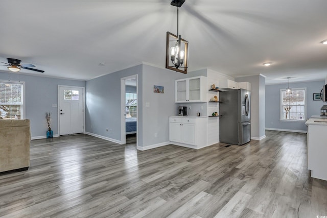 kitchen with ceiling fan with notable chandelier, wood finished floors, white cabinets, open floor plan, and stainless steel fridge