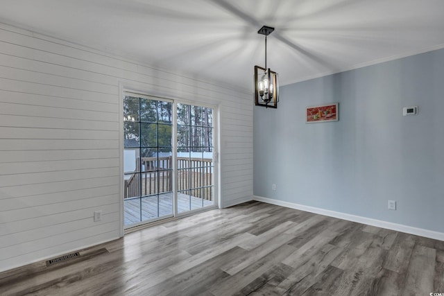 interior space with a notable chandelier, crown molding, wooden walls, wood finished floors, and baseboards