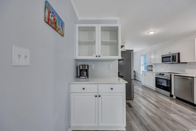 kitchen featuring stainless steel appliances, white cabinetry, light wood finished floors, glass insert cabinets, and crown molding