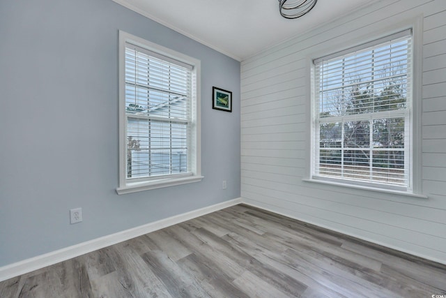 empty room featuring baseboards, wooden walls, wood finished floors, and crown molding