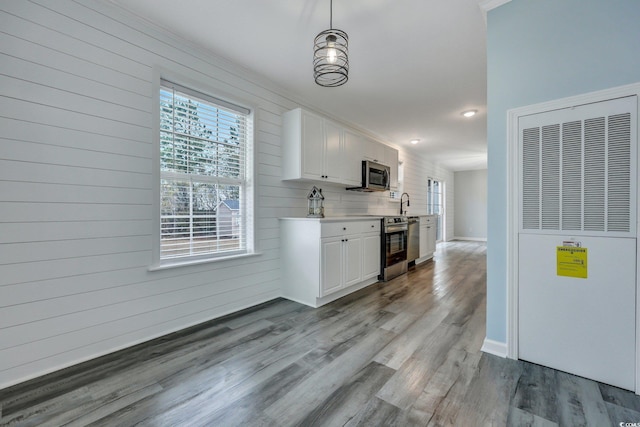 kitchen with light countertops, appliances with stainless steel finishes, white cabinetry, a sink, and wood finished floors