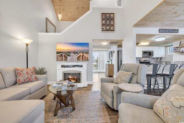 living room with sink, a towering ceiling, wood-type flooring, and wooden ceiling