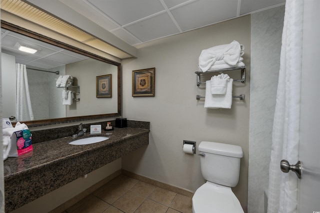 bathroom with tile patterned floors, toilet, sink, and a drop ceiling