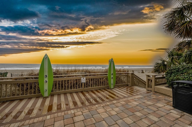 patio terrace at dusk featuring a view of the beach and a water view