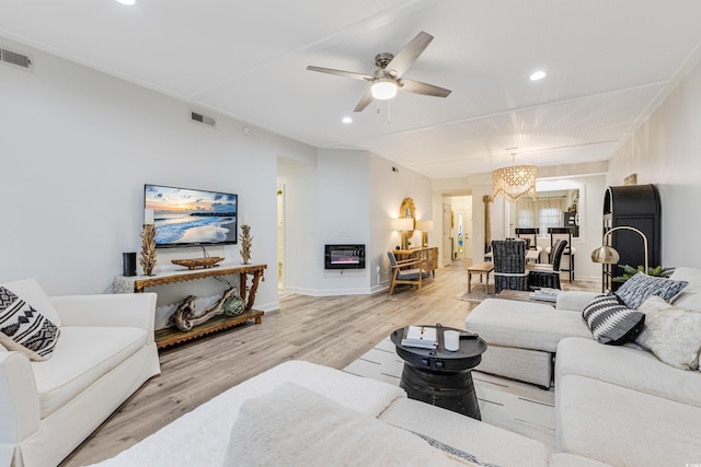 living room with heating unit, ceiling fan with notable chandelier, and light hardwood / wood-style flooring