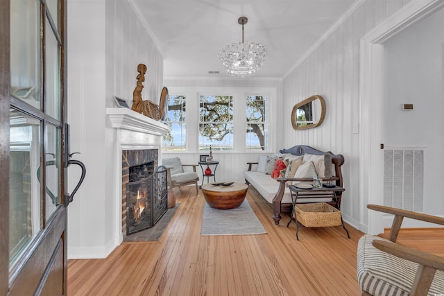 sitting room with a notable chandelier, a fireplace, visible vents, light wood-style floors, and ornamental molding