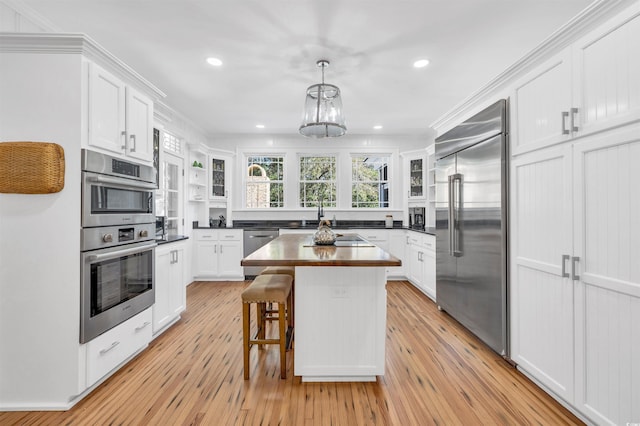 kitchen featuring stainless steel appliances, wood counters, white cabinetry, and decorative light fixtures