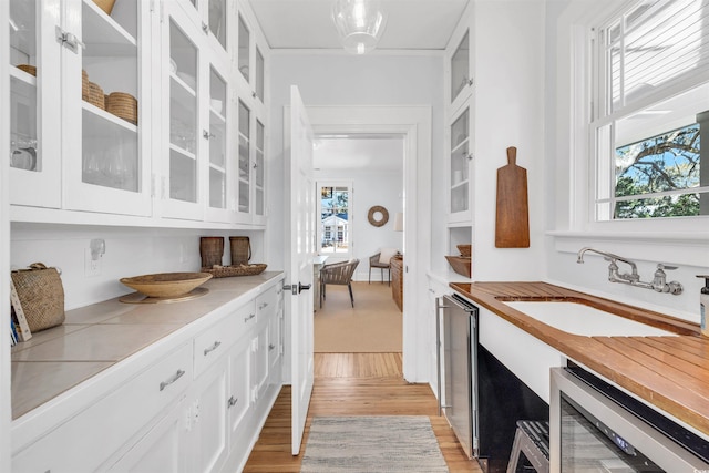 kitchen with beverage cooler, a sink, white cabinets, light countertops, and glass insert cabinets