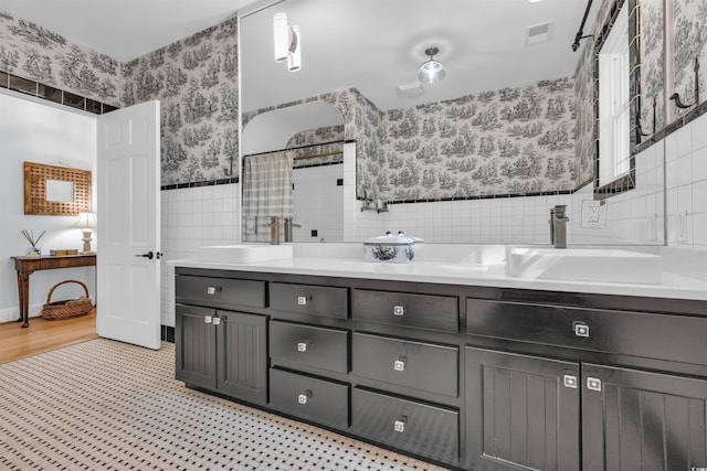bathroom featuring a wainscoted wall, a sink, tile walls, and wallpapered walls