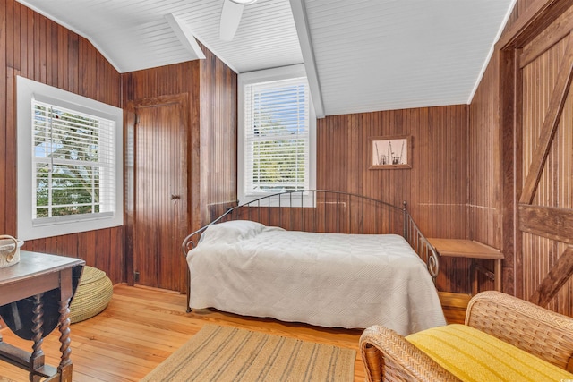 bedroom featuring lofted ceiling, light wood-style floors, wooden walls, and multiple windows