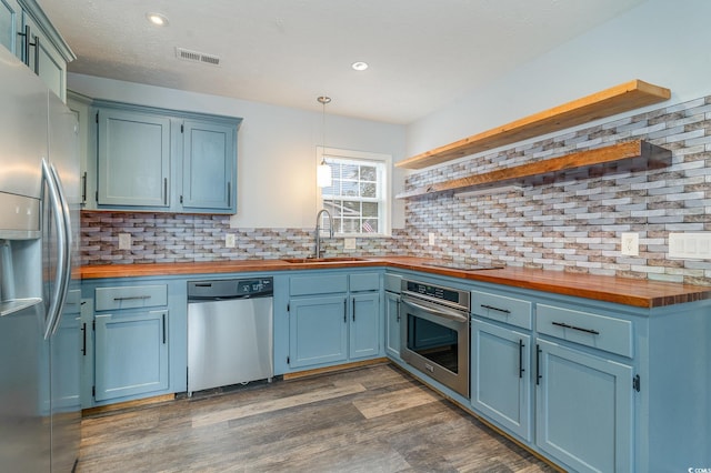 kitchen with blue cabinetry, wood counters, appliances with stainless steel finishes, and sink