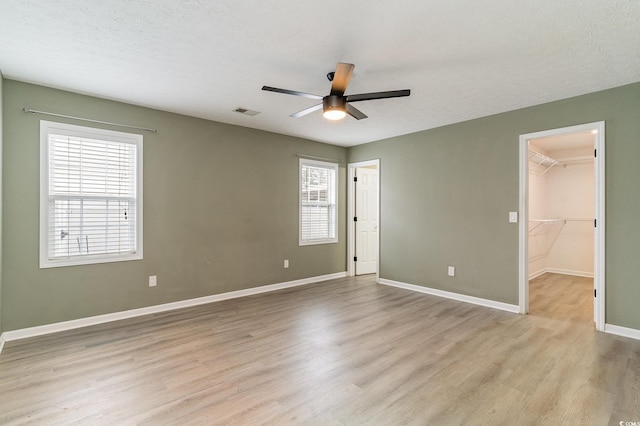 spare room featuring a walk in closet, a textured ceiling, light wood-type flooring, a closet, and ceiling fan