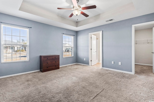 unfurnished bedroom with a raised ceiling, light carpet, a walk in closet, and a closet