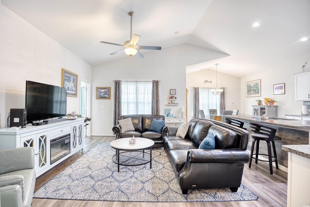 living room featuring lofted ceiling, sink, ceiling fan with notable chandelier, and light wood-type flooring