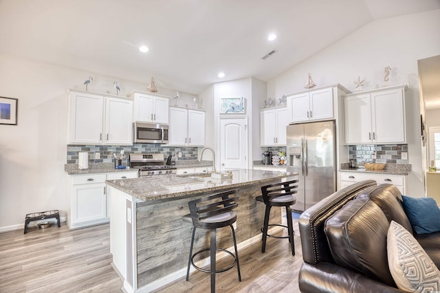 kitchen featuring sink, white cabinets, a kitchen bar, light stone counters, and stainless steel appliances