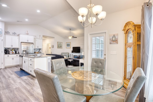 dining space with vaulted ceiling, sink, ceiling fan with notable chandelier, and light hardwood / wood-style flooring