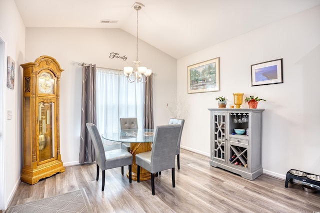 dining space with an inviting chandelier, hardwood / wood-style flooring, and vaulted ceiling