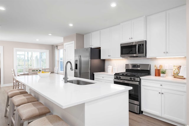 kitchen with a center island with sink, a breakfast bar, stainless steel appliances, light countertops, and a sink