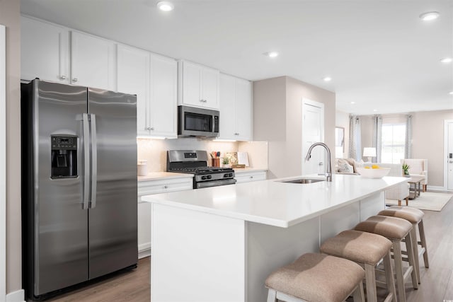 kitchen with a sink, a center island with sink, stainless steel appliances, and light countertops