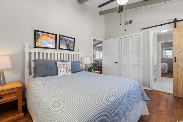 bedroom with a closet, beamed ceiling, ceiling fan, dark hardwood / wood-style flooring, and a barn door