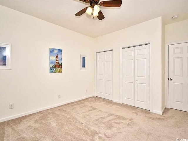 unfurnished bedroom with ceiling fan, light colored carpet, and multiple closets