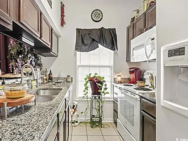 kitchen featuring sink, light tile patterned floors, dark brown cabinetry, light stone counters, and white appliances