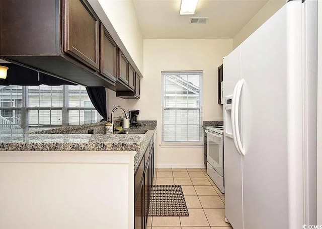 kitchen with sink, dark brown cabinets, light tile patterned floors, white appliances, and dark stone counters