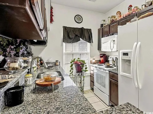 kitchen with sink, white appliances, light tile patterned floors, stone counters, and dark brown cabinetry