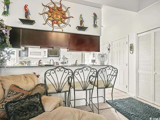 kitchen with light tile patterned floors, white appliances, dark brown cabinets, and kitchen peninsula