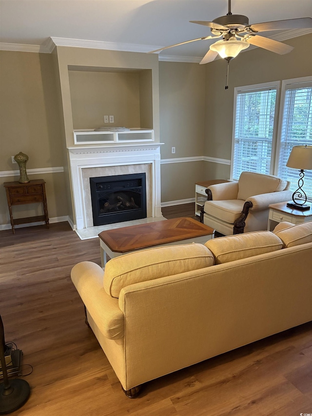 living room featuring a premium fireplace, wood-type flooring, ornamental molding, and ceiling fan