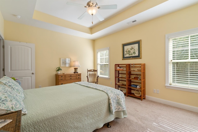 carpeted bedroom featuring ceiling fan, a raised ceiling, and multiple windows