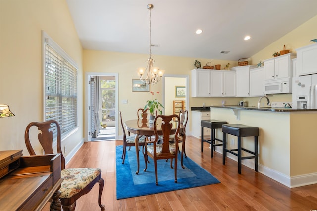 dining area with lofted ceiling, hardwood / wood-style floors, sink, and a chandelier