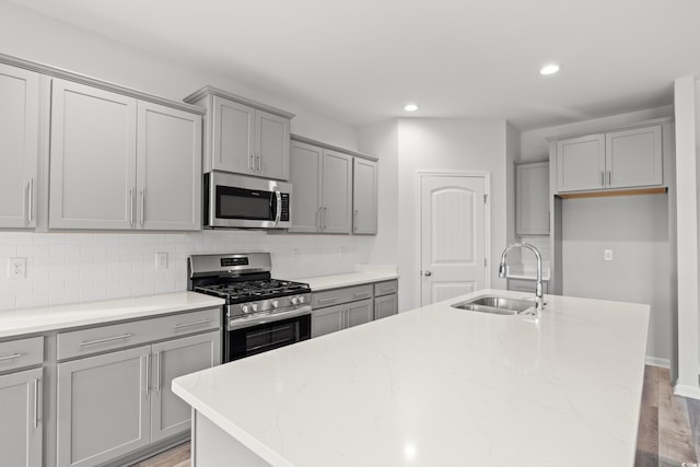 kitchen with backsplash, light stone countertops, a kitchen island with sink, stainless steel appliances, and a sink