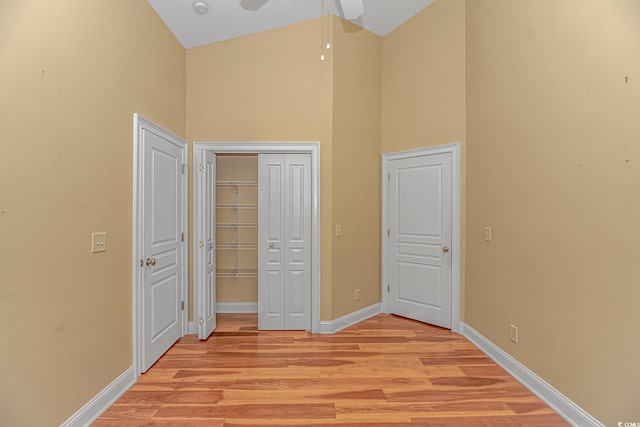 unfurnished bedroom with high vaulted ceiling, a closet, baseboards, and light wood finished floors