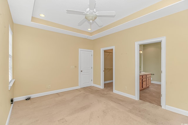 unfurnished bedroom featuring a tray ceiling, light carpet, baseboards, and multiple windows