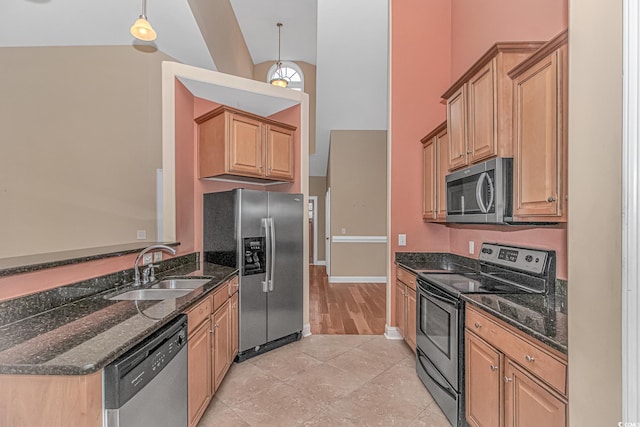 kitchen with stainless steel appliances, a sink, hanging light fixtures, and dark stone countertops