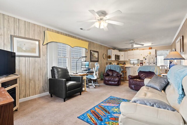 living room with baseboards, a ceiling fan, crown molding, wooden walls, and light colored carpet