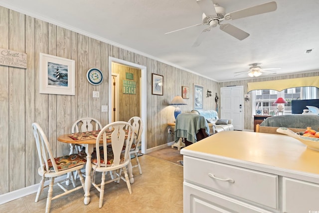 dining area featuring wooden walls, ornamental molding, ceiling fan, and baseboards