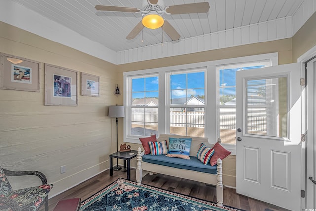 sitting room with a ceiling fan, wood walls, baseboards, and wood finished floors