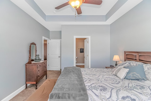 bedroom featuring light carpet, baseboards, a ceiling fan, ensuite bath, and a tray ceiling