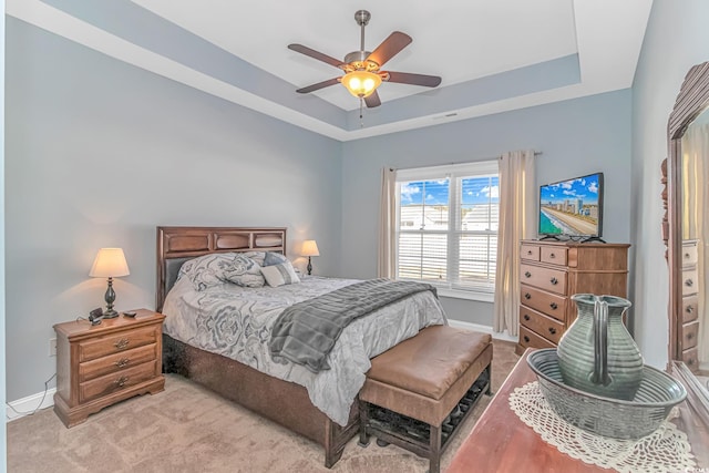 bedroom featuring light carpet, baseboards, a raised ceiling, and a ceiling fan